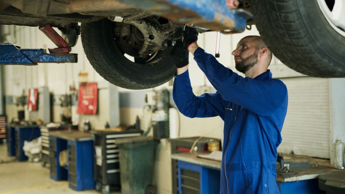 A mechanic inspecting the undercarriage and frame of a lifted car in a workshop