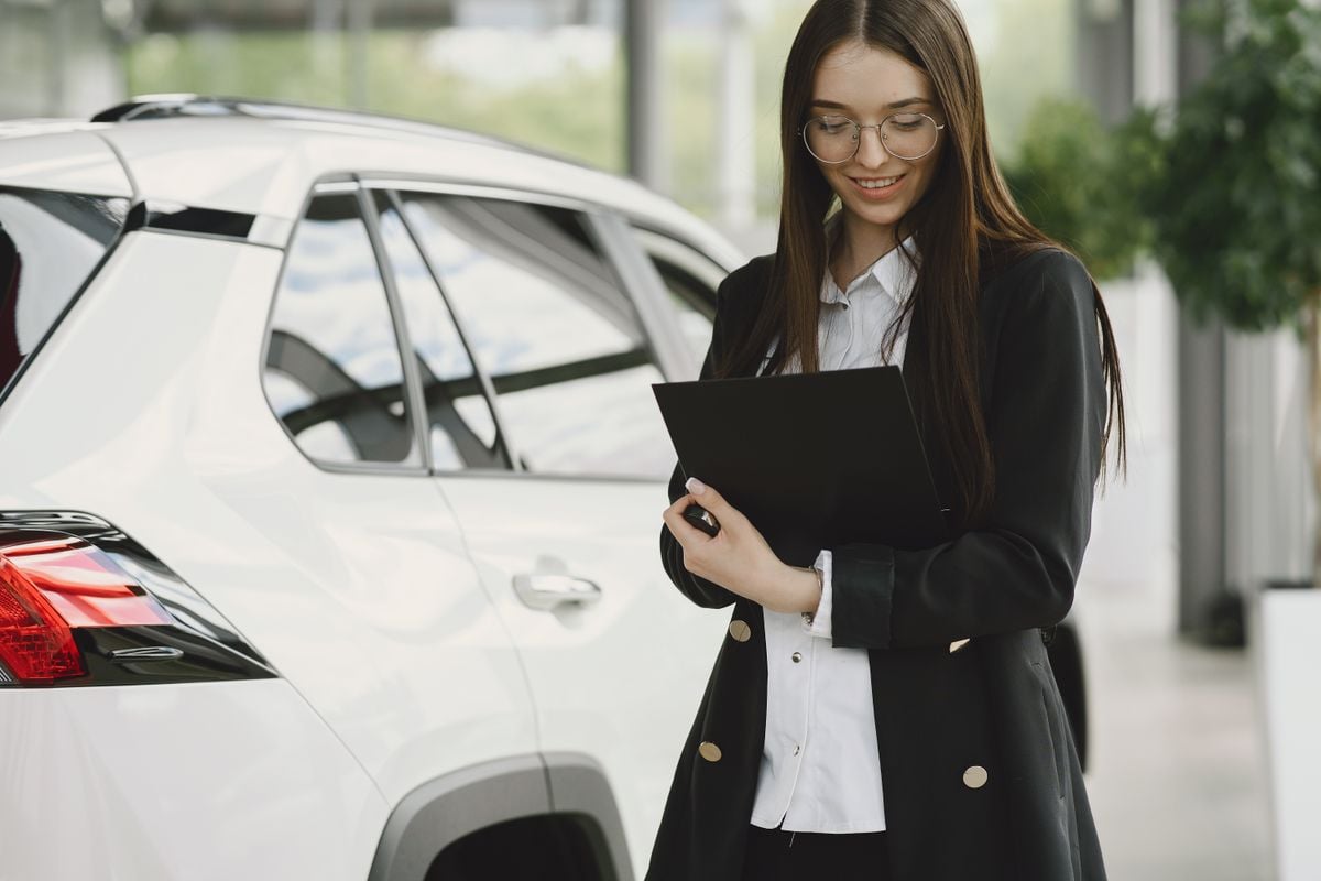 A person reviewing vehicle title and purchase documents beside a car