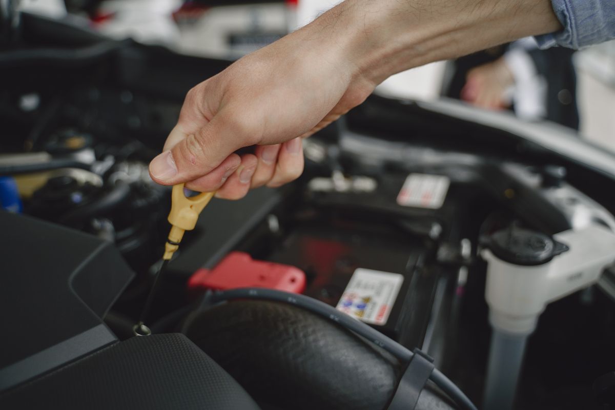A hand pulling the oil dipstick in an open engine bay to check fluid level and color