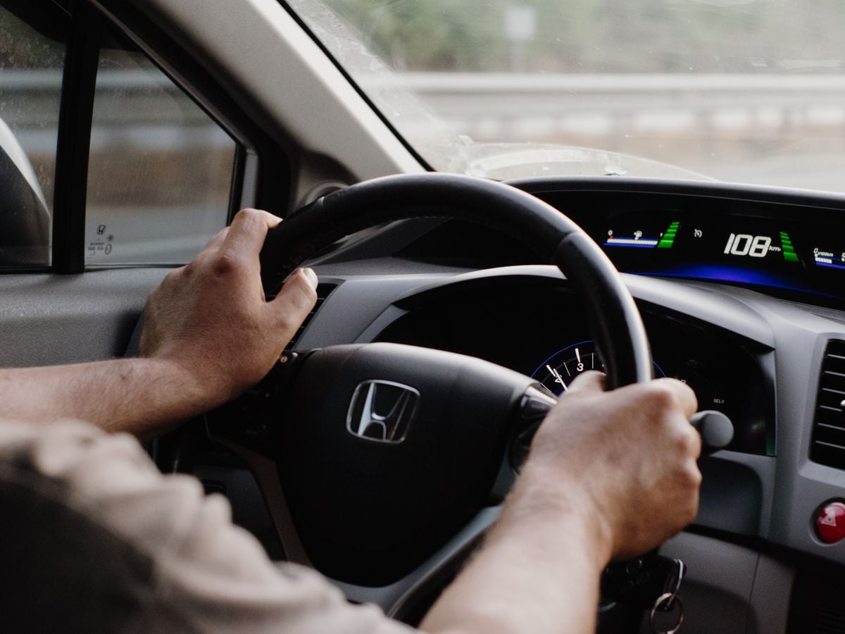 Driver's hands on the steering wheel during a test drive with the road visible through the windshield