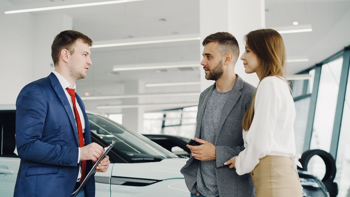 A salesperson walking a couple through their options beside a car at a dealership