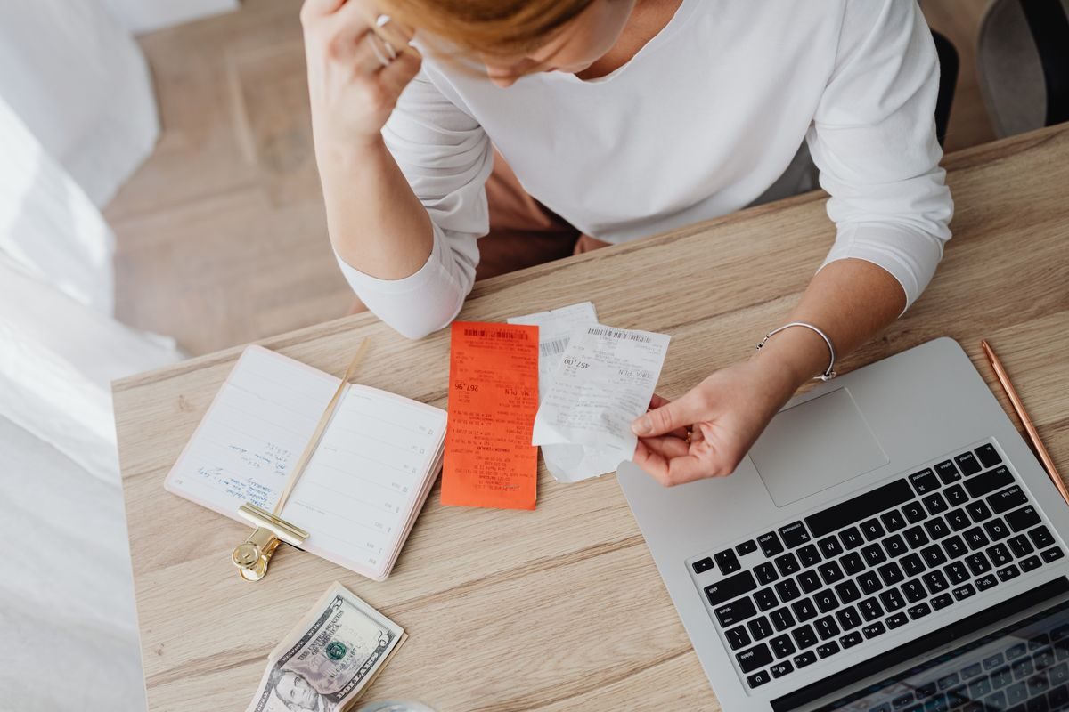 A person reviewing personal finances and bills at a laptop to work out a car budget