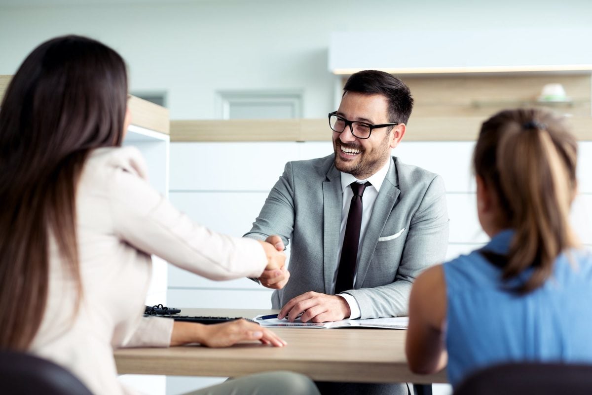Buyer and finance manager shaking hands over in-house car financing paperwork