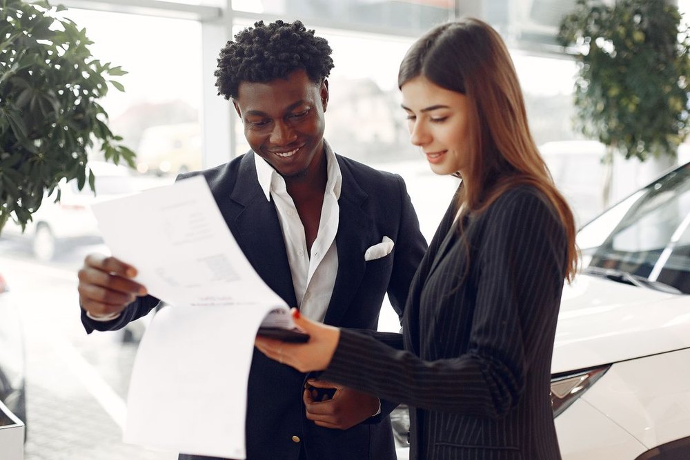 A car buyer and a dealership staff member going through financing paperwork together beside a vehicle
