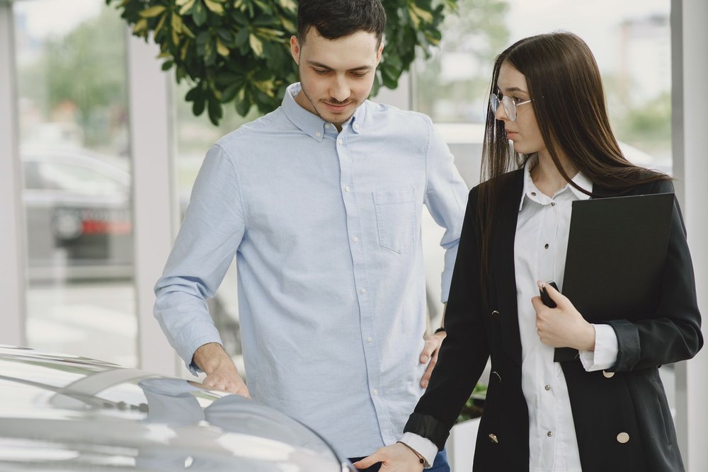A car owner and a dealership staff member with a clipboard looking over a vehicle together during a trade-in appraisal